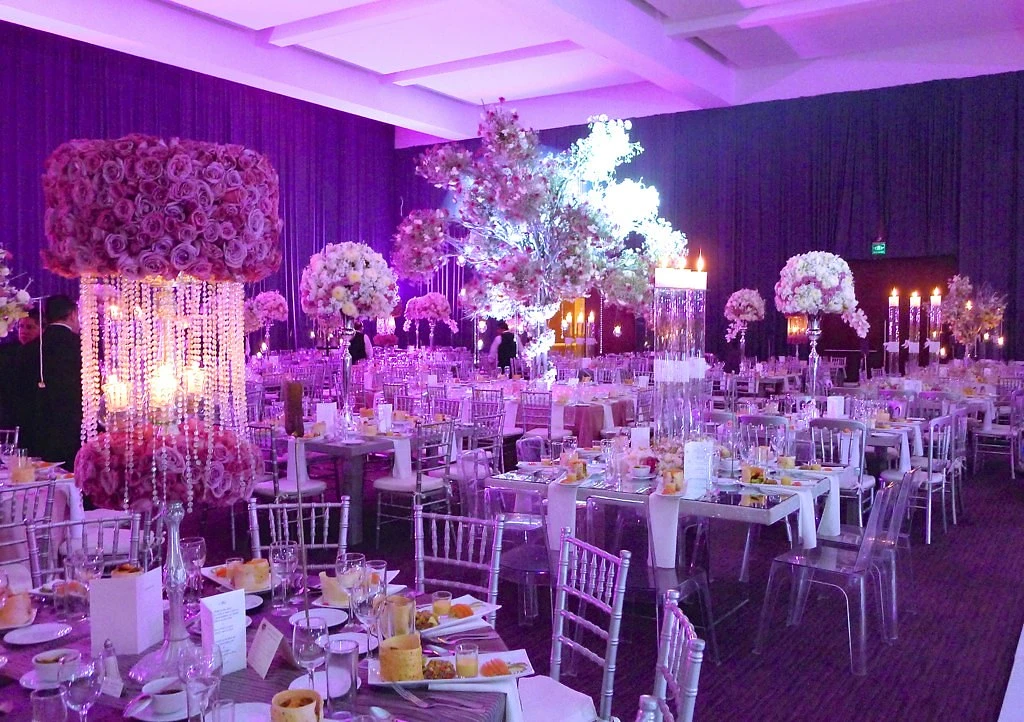 Salón de boda con iluminación violeta y grandes arreglos florales